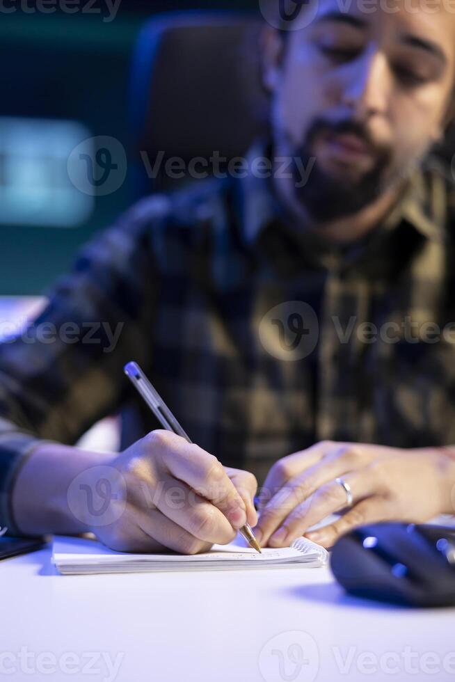 selektiv fokus av manlig bloggare skrivning ner ny idéer, planera ny innehåll. man Sammanträde på tabell är använder sig av en penna och anteckningsbok för handskriven anteckningar av hans forskning arbete. foto