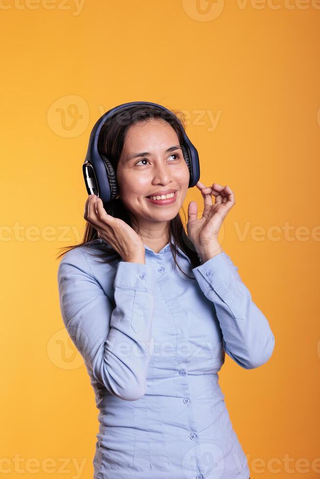 glad filippinare kvinna lyssnande musik och dans, njuter fri tid i studio över gul bakgrund. attraktiv modell bär hörlurar som visar rolig dansa rör sig. underhållning begrepp foto