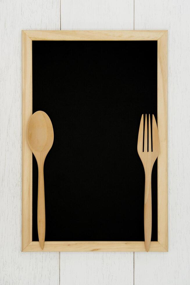 tom svarta tavlan med trä- sked och gaffel på vit trä planka bakgrund. styled stock fotografi för kokbok, mat blog inlägg och social media innehåll. foto