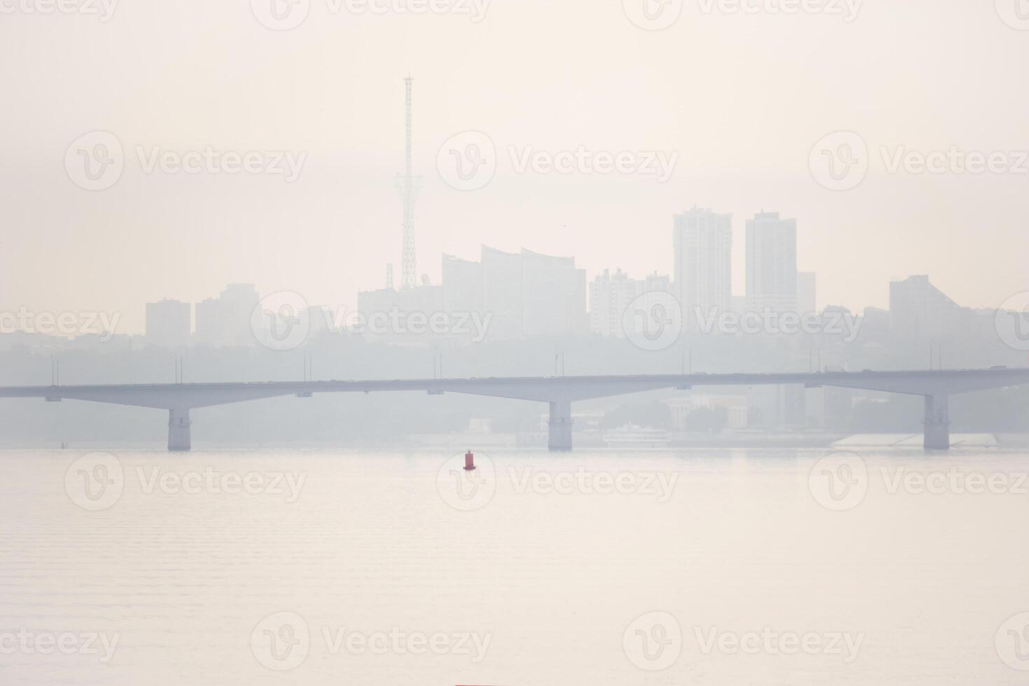 väg bro över en bred flod och de silhuett av en avlägsen stad Bakom den i de morgon- dimma foto