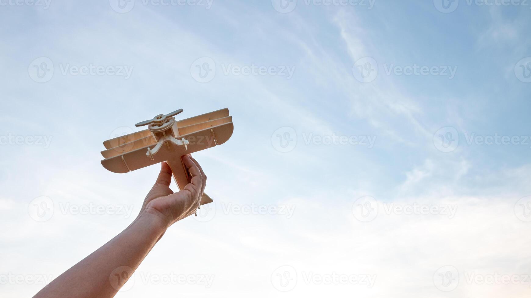 barn innehav en trä- flygplan modell hög i de himmel foto