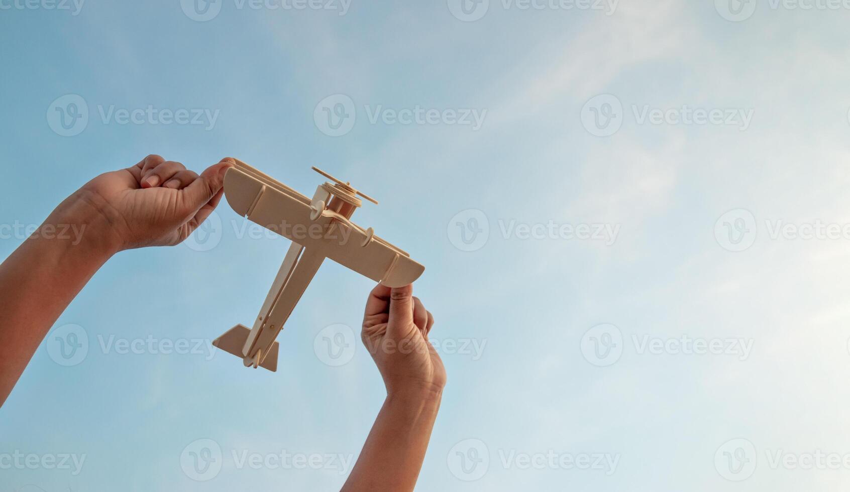 barn innehav en trä- flygplan modell hög i de himmel foto