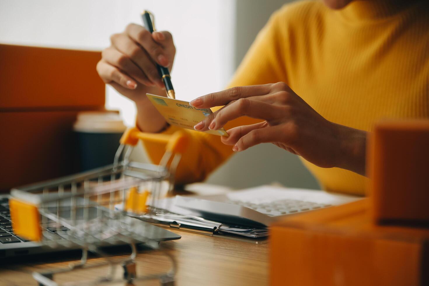 ung kvinna innehav en smartphone, läsplatta som visar betalning Framgång och kreditera kort med gul paket låda som uppkopplad handla begrepp i kontor foto