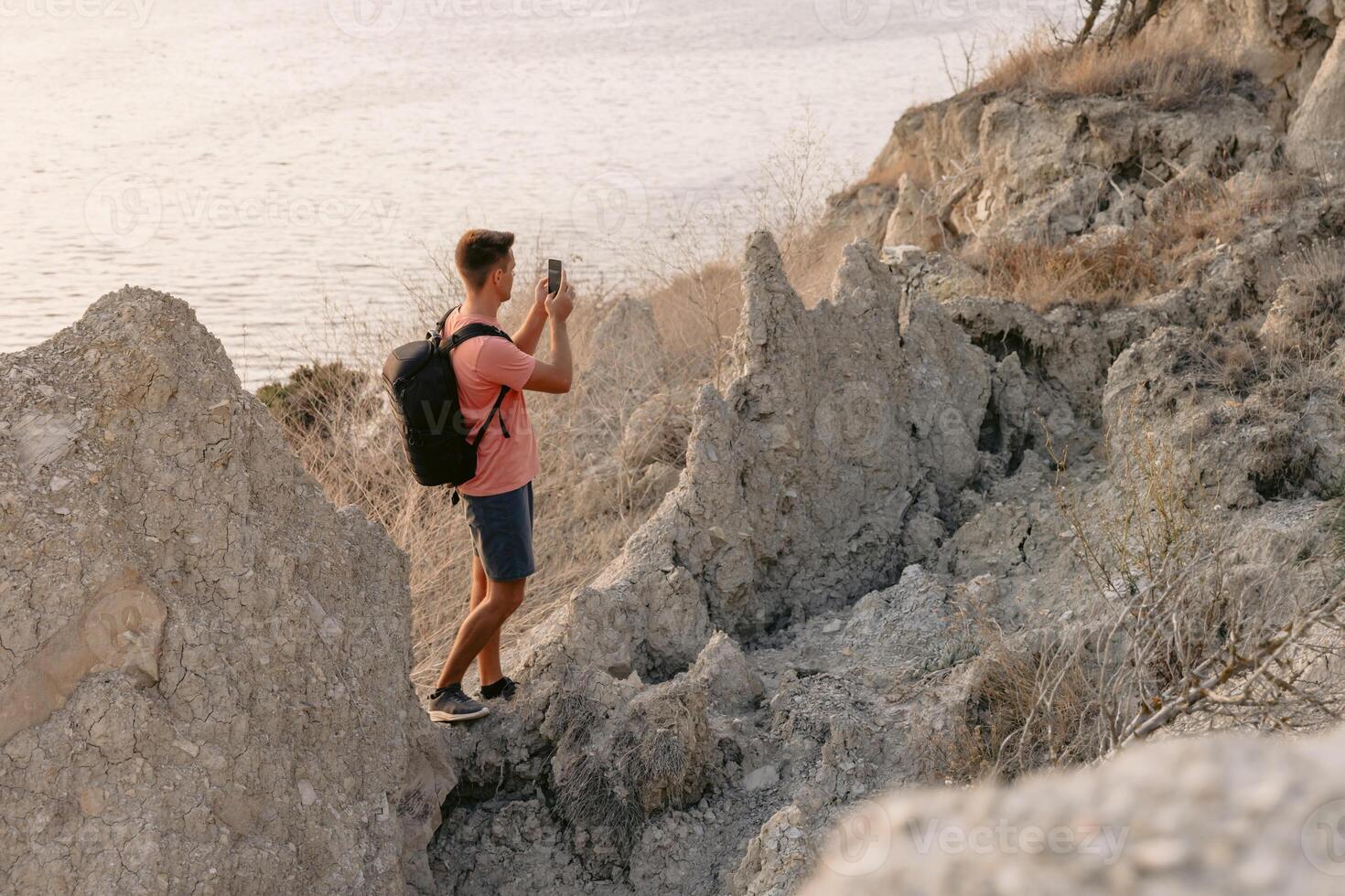 vandrare vistas på de sten på kustlinje med värma solnedgång ljus. resande man med smartphone i utomhus. foto
