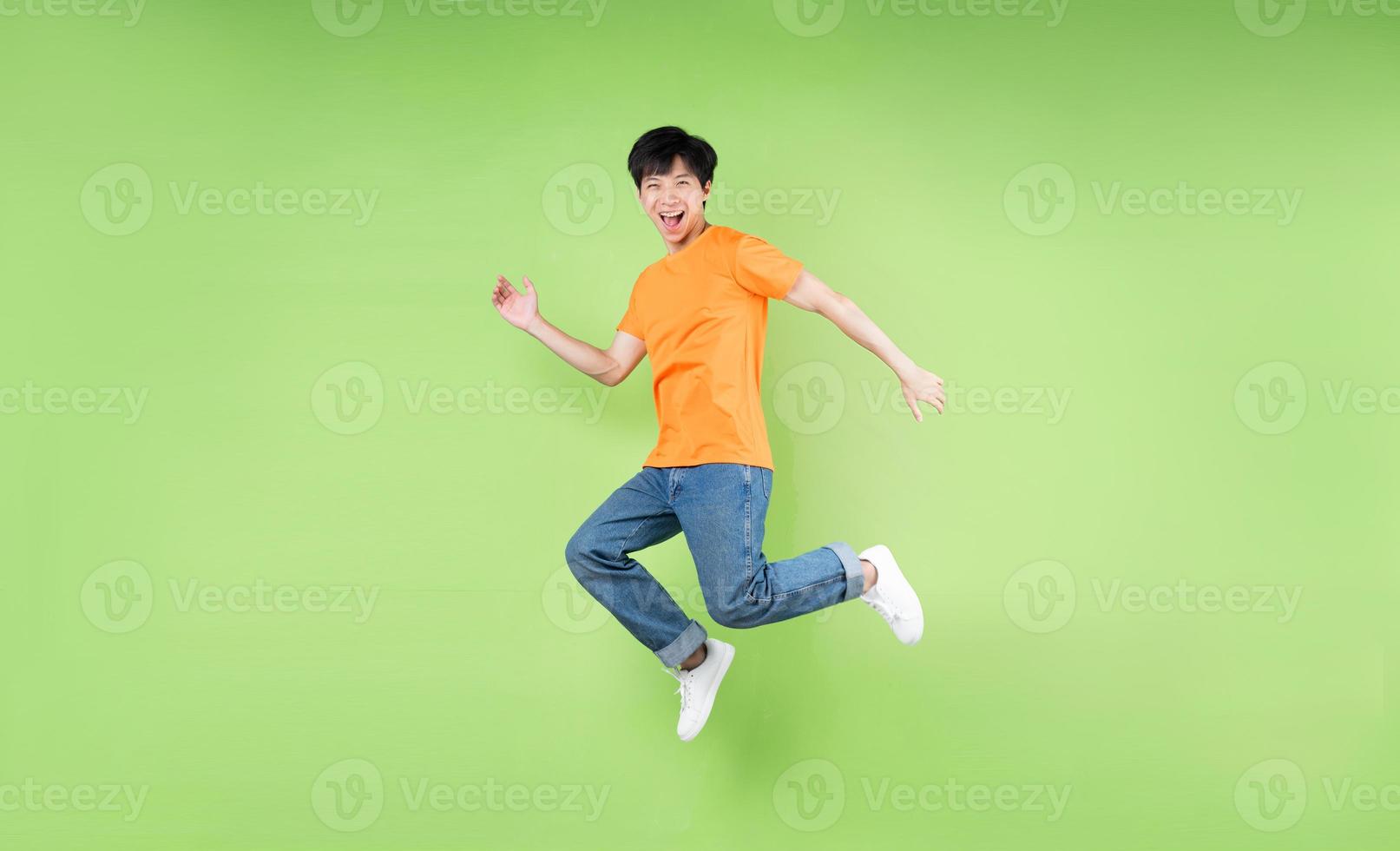 ung asiatisk man som hoppar, isolerad på grön bakgrund foto