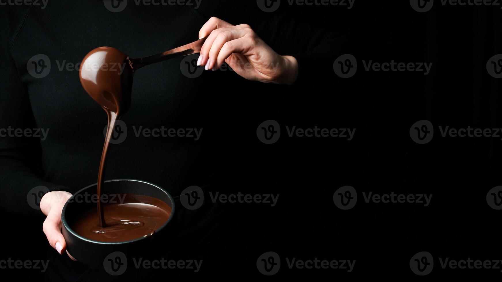 de kock skopor varm choklad in i en skål. på en svart bakgrund. förberedelse av choklad. foto