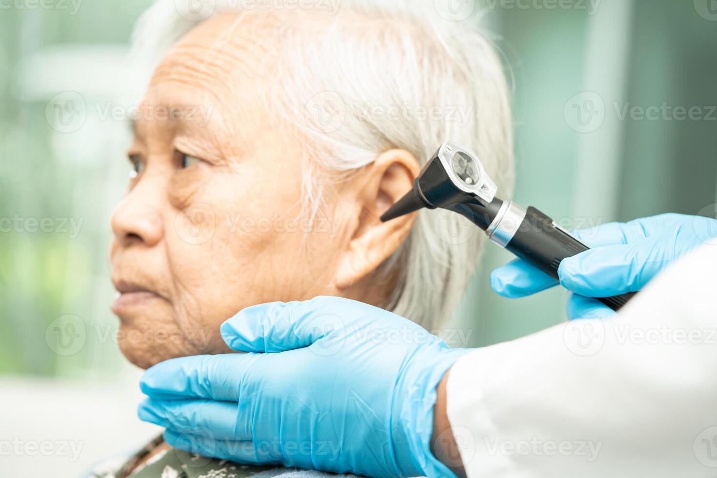audiologist eller ent läkare använda sig av otoskop kontroll öra av asiatisk senior kvinna patient behandla hörsel förlust problem. foto