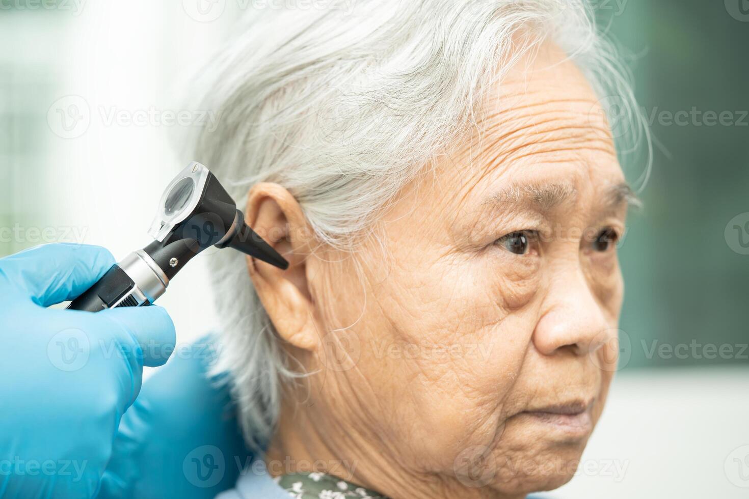 audiologist eller ent läkare använda sig av otoskop kontroll öra av asiatisk senior kvinna patient behandla hörsel förlust problem. foto