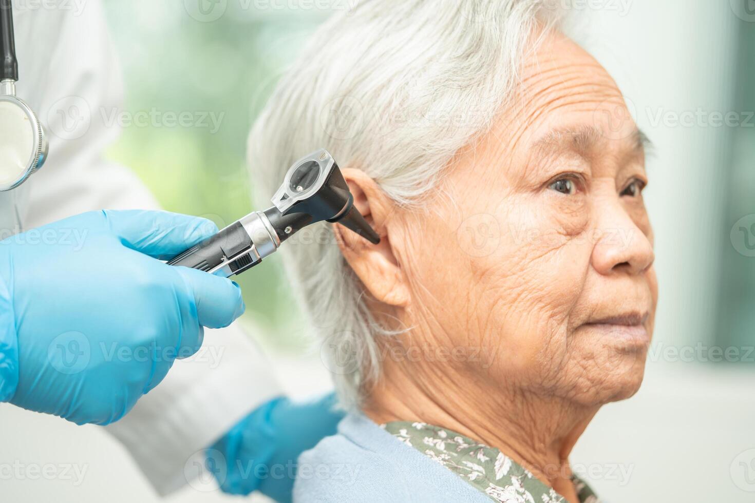 audiologist eller ent läkare använda sig av otoskop kontroll öra av asiatisk senior kvinna patient behandla hörsel förlust problem. foto