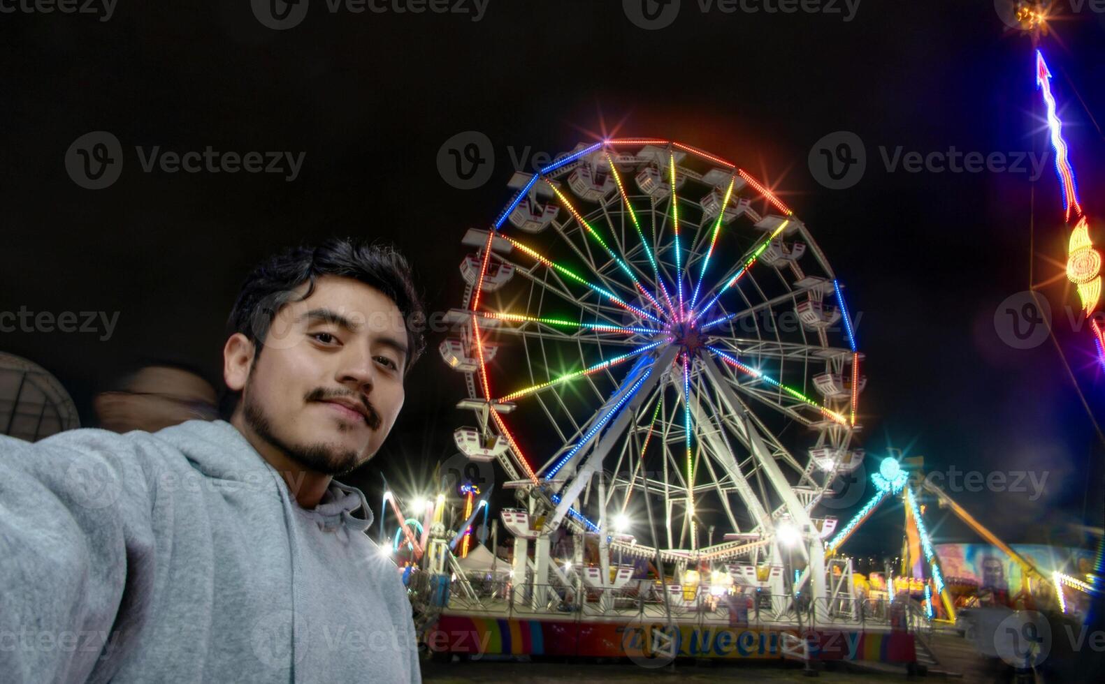 man tar selfie på mexikansk rättvis med ferris hjul och färgrik lampor på natt foto