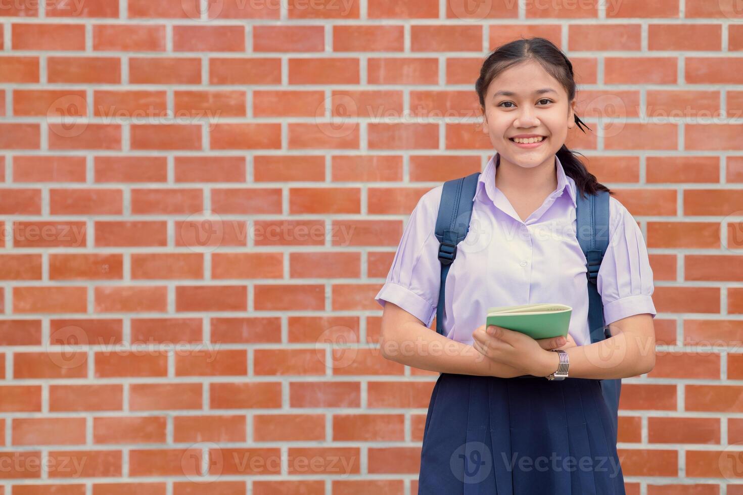thai asiatisk skola flicka tonåring Lycklig leende i enhetlig hantera bok och skola väska med kopia Plats foto