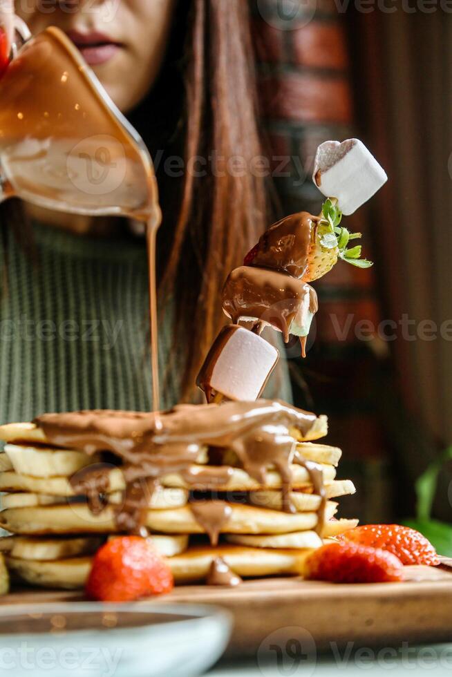 kvinna häller sirap på en stack av pannkakor foto