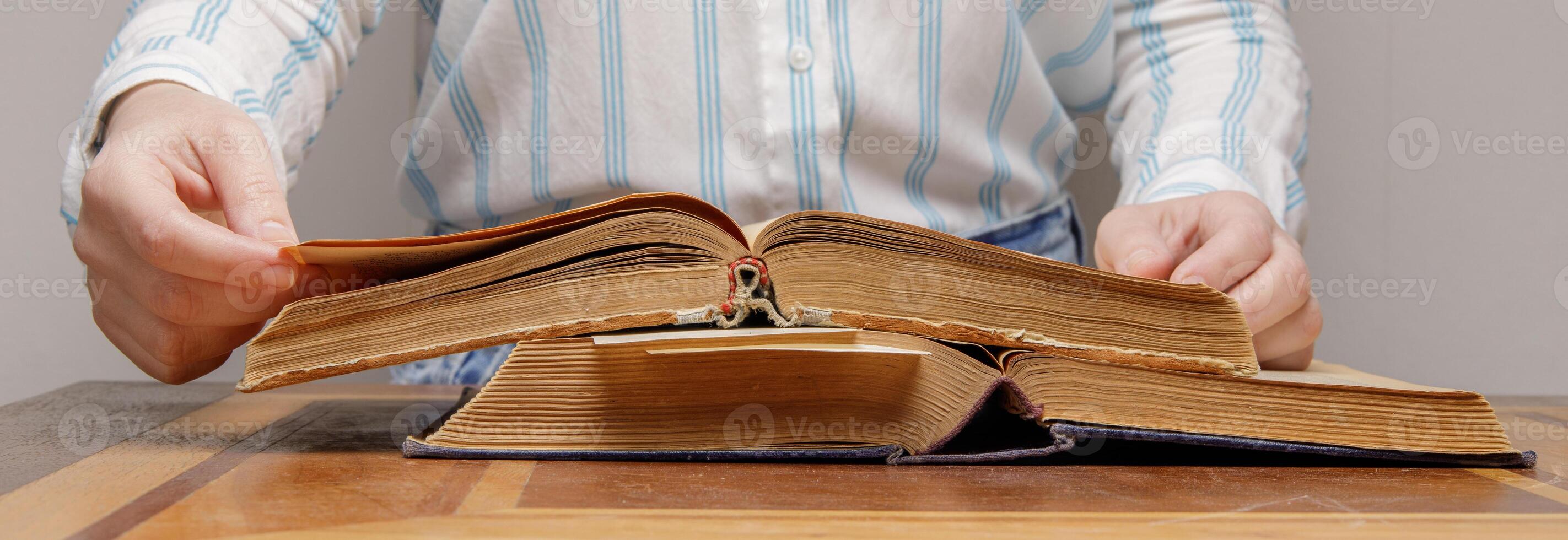 de händer av ett osynlig person blad genom de sidor av ett gammal bok liggande på en trä- tabell i en universitet eller skola bibliotek. foto