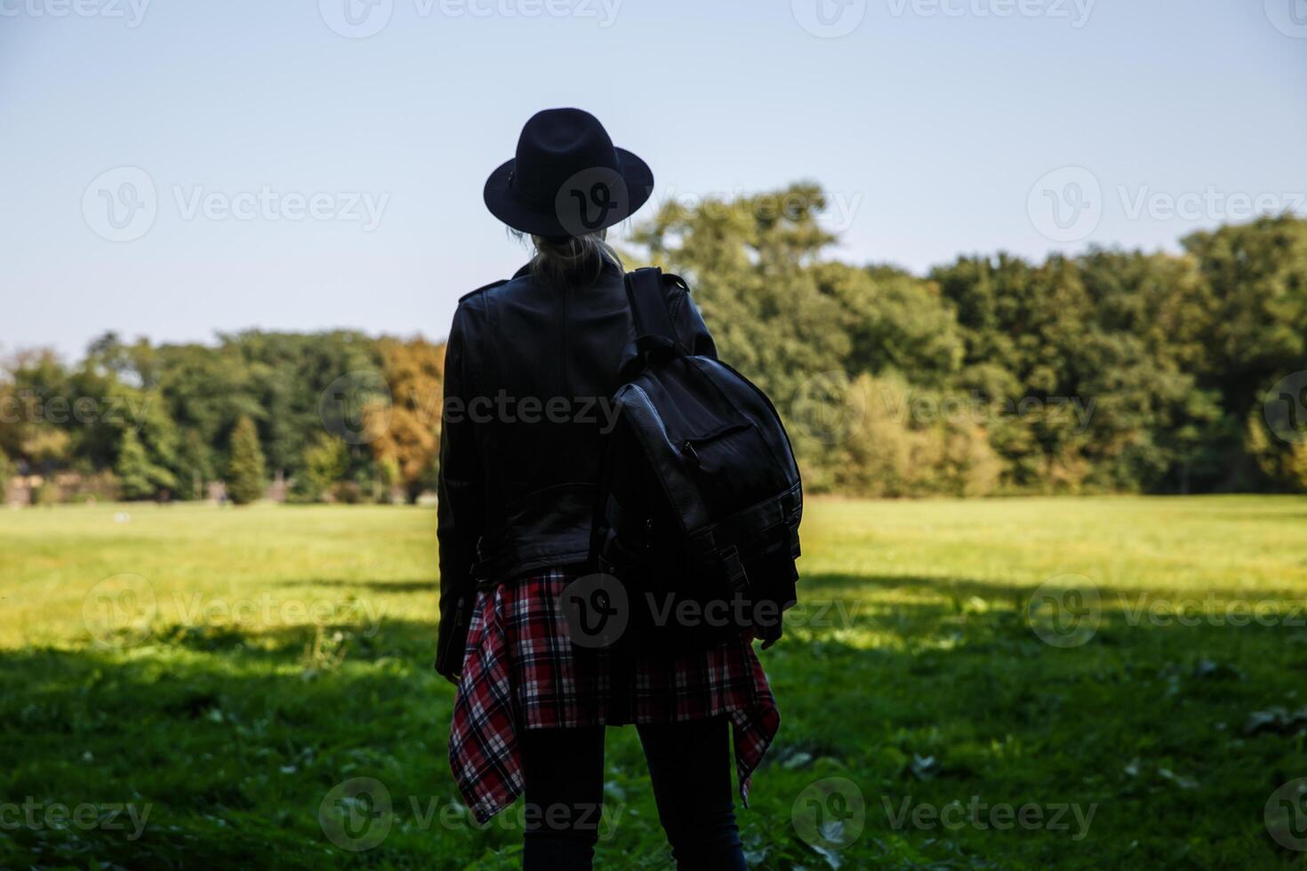 ung caucasian kvinna med en ryggsäck och hatt i de skugga av träd nära de fält. bakgrund, stänga upp. selektiv fokus.hög kvalitet Foto