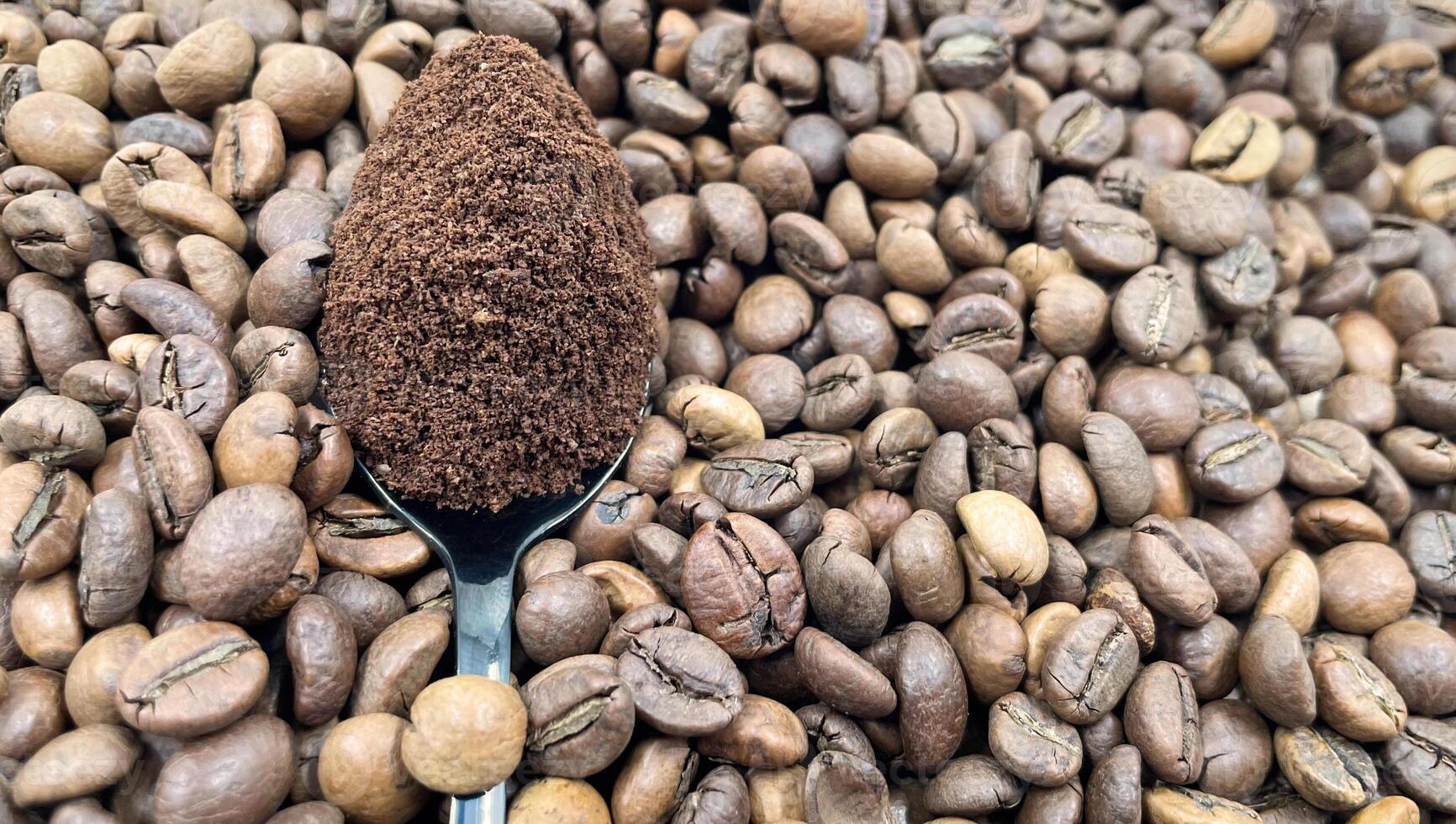 mot de bakgrund av rostad aromatisk kaffe bönor lögner en metall sked fylld med jord kaffe. en dryck tillverkad från rostad och jord bönor från de kaffe träd eller kaffe buske. foto