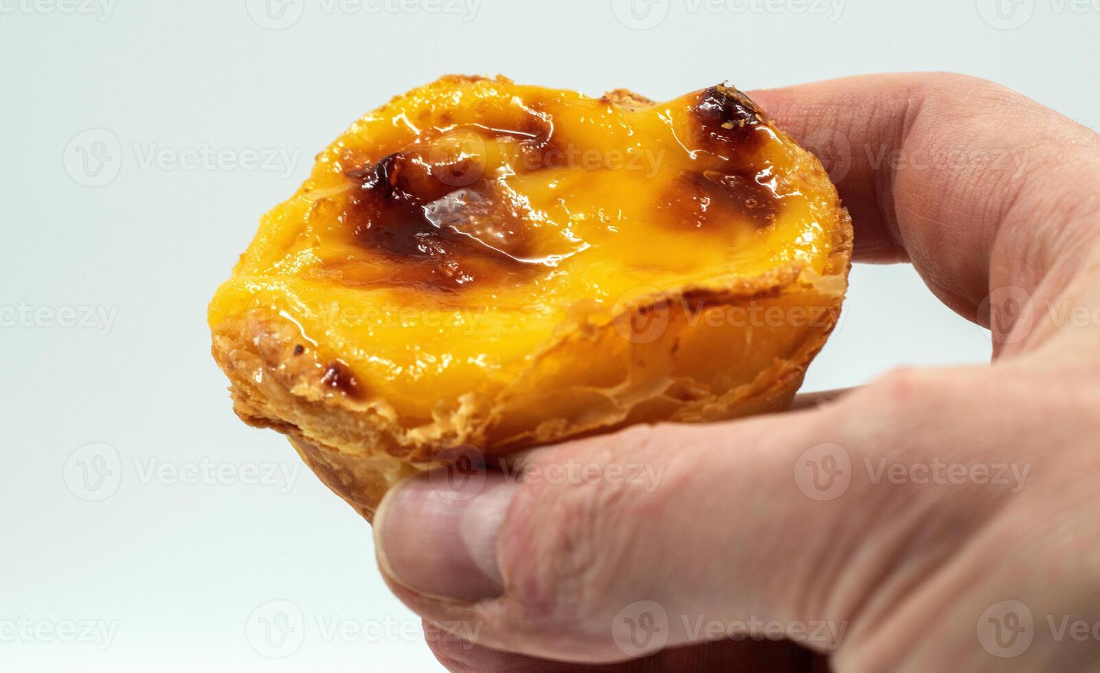 en mannens hand innehar ett portugisiska pastell de nata paj med tjock vaniljsås och kanel pinnar på en vit bakgrund. pastell de belem är en bakverk med en bränd topp och en Krispig puff bakverk skorpa. foto