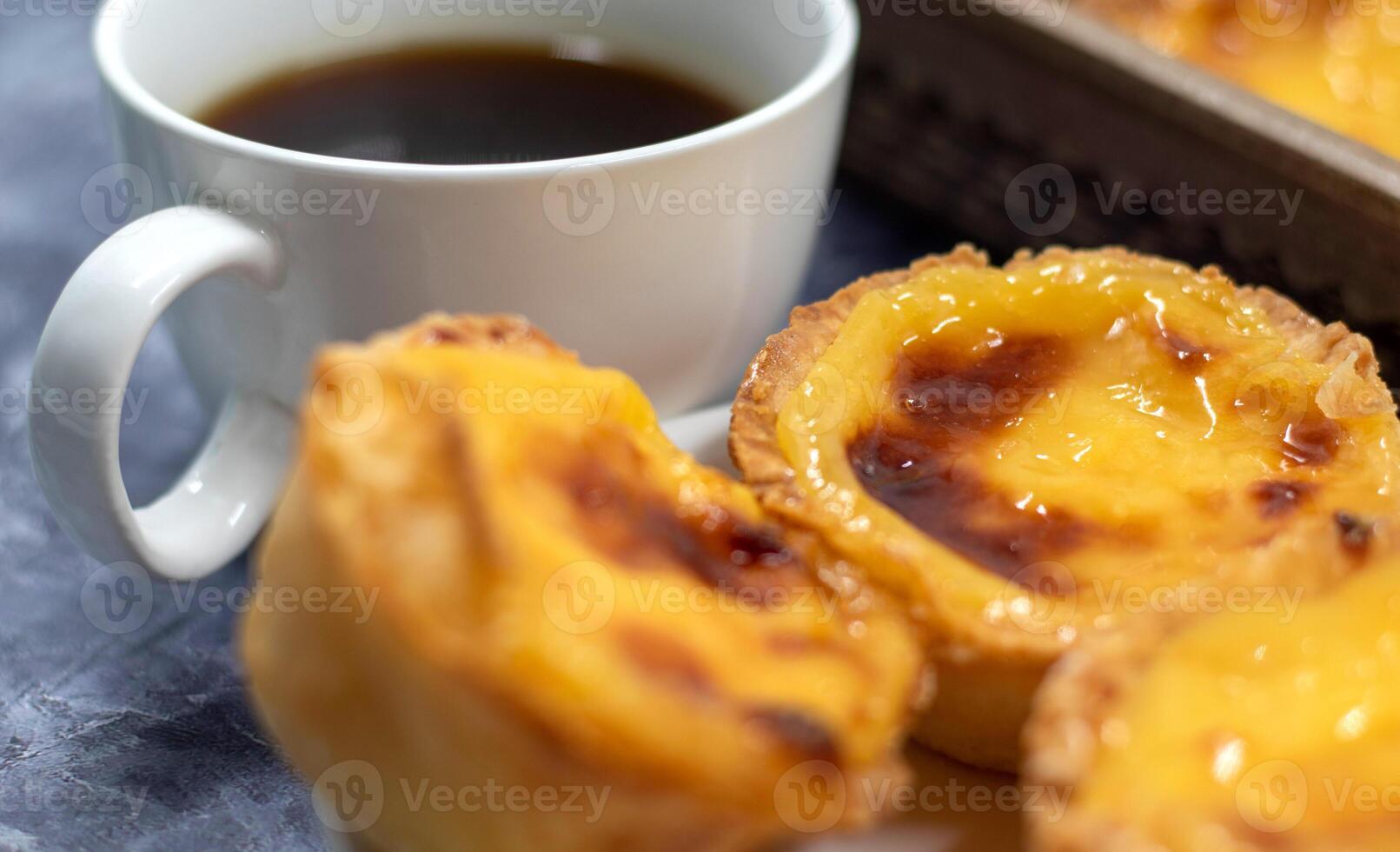 massor av desserter pastell de nata eller portugisiska ägg syrlig med en vit kopp av svart kaffe. pastell de belm är en små paj med en Krispig puff bakverk skorpa och en tjock vaniljsås grädde fyllning. foto