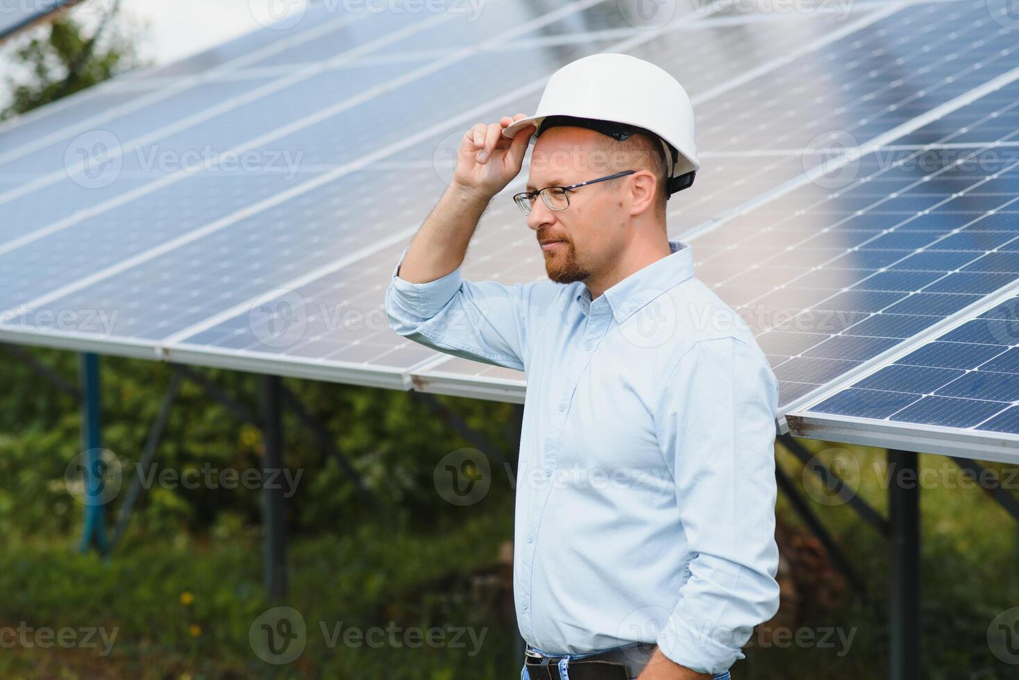 porträtt av manlig ingenjör med läsplatta i hans händer nära de sol- paneler station, bär hjälm på solig dag. grön ekologisk kraft energi generation. foto