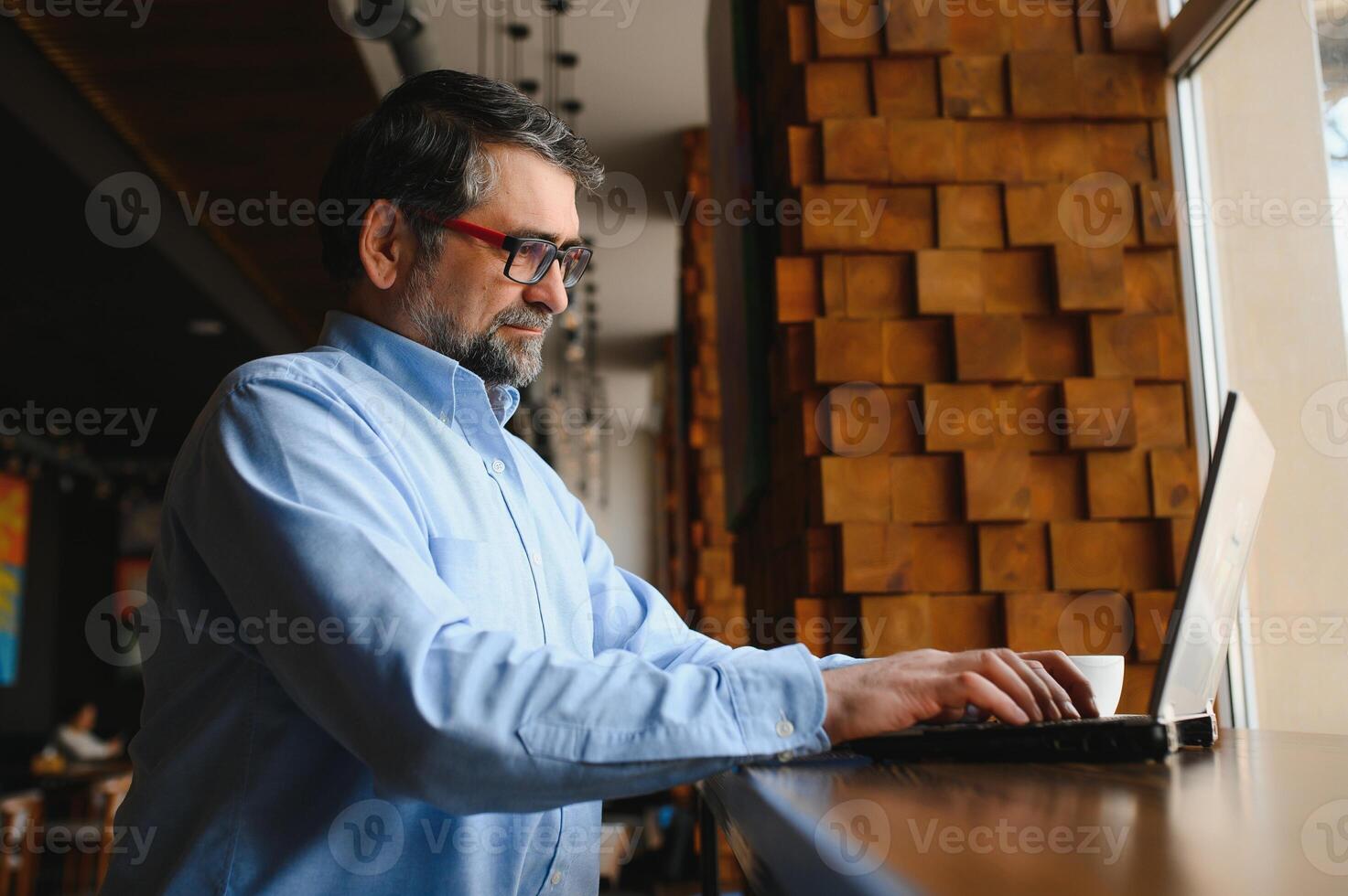 mogna affärsman dricka kaffe i Kafé. porträtt av stilig man bär eleganta glasögon använder sig av bärbar dator, ser på kamera, leende. kaffe ha sönder begrepp foto
