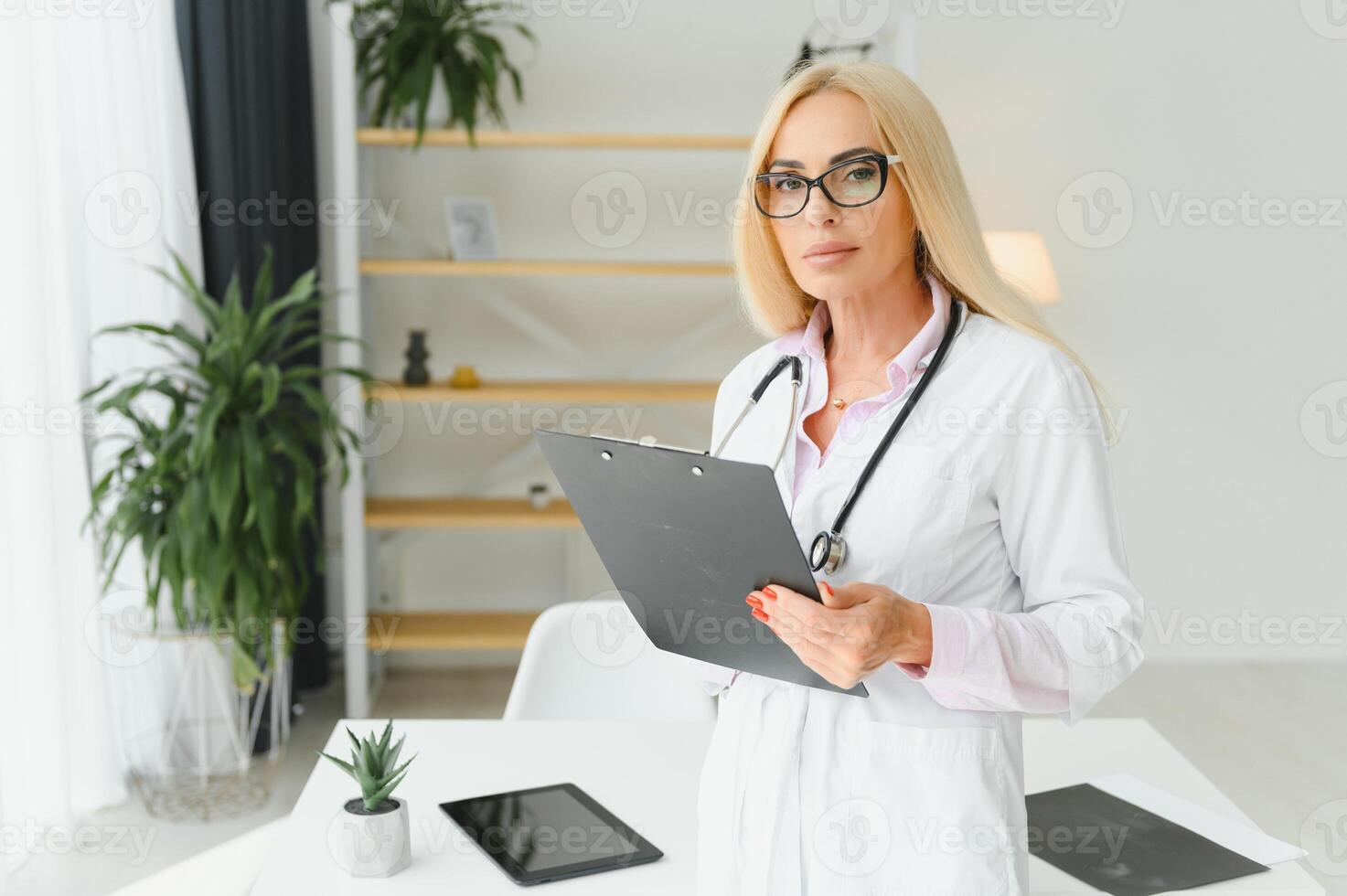 kvinna läkare bär labb täcka och stetoskop och innehav Urklipp i henne händer medan stående på sjukhus. foto