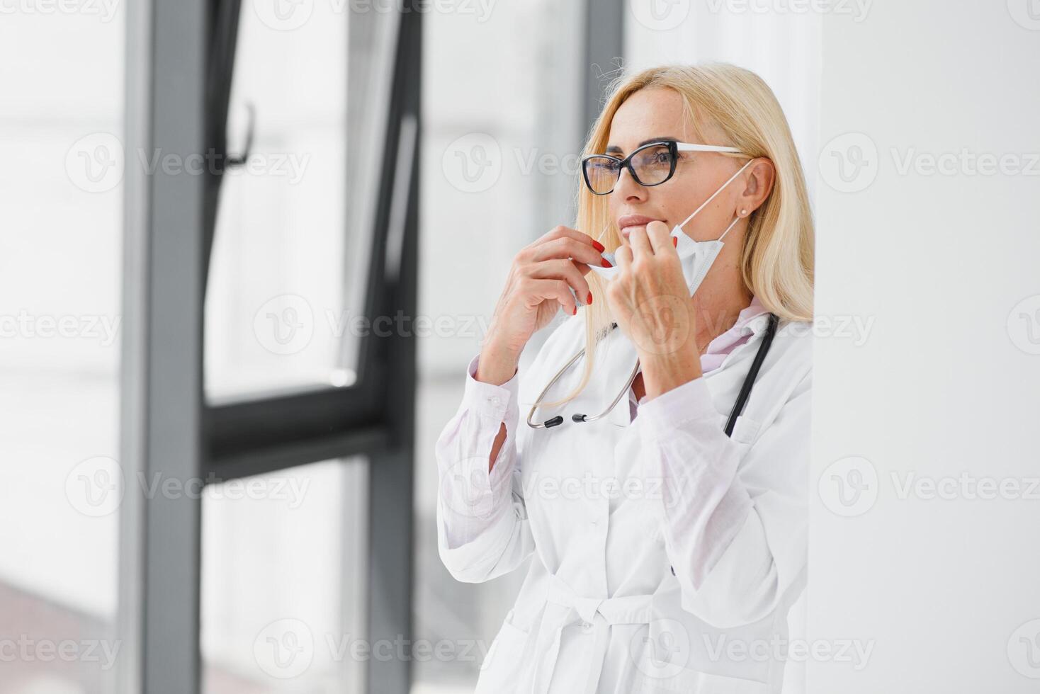 kvinna läkare bär labb täcka och stetoskop och innehav Urklipp i henne händer medan stående på sjukhus. foto
