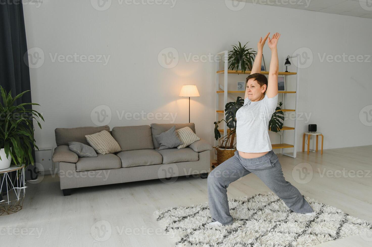 mitten ålder kvinna leende Lycklig håller på med övning och stretching på Hem foto