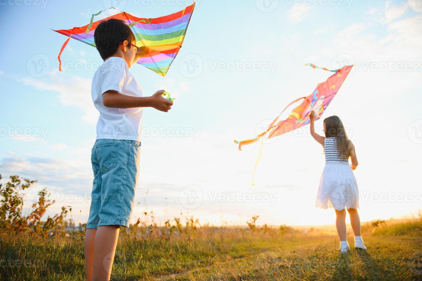 Lycklig barn lansera en drake i de fält på solnedgång. liten pojke och flicka på sommar semester. foto