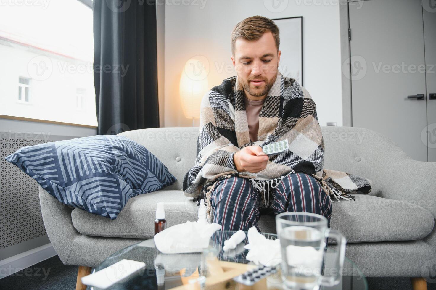 en sjuk man sitter på Hem på en grå soffa med en filt. sjukdom, skydd, coronavirus, sjukdom, influensa foto