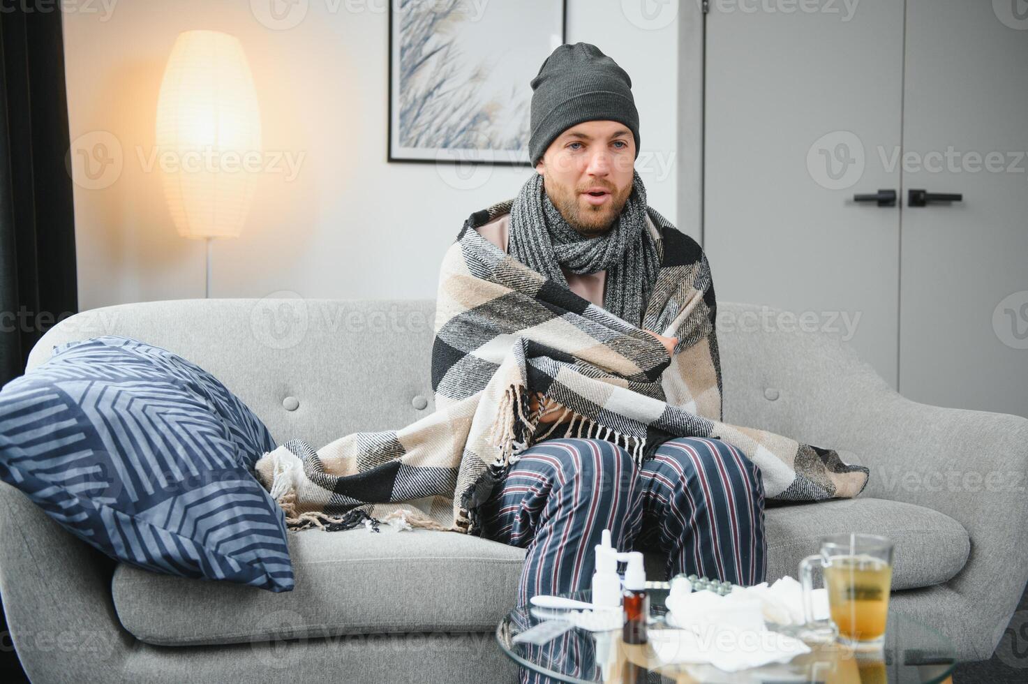 en sjuk man sitter på Hem på en grå soffa med en filt. sjukdom, skydd, coronavirus, sjukdom, influensa foto