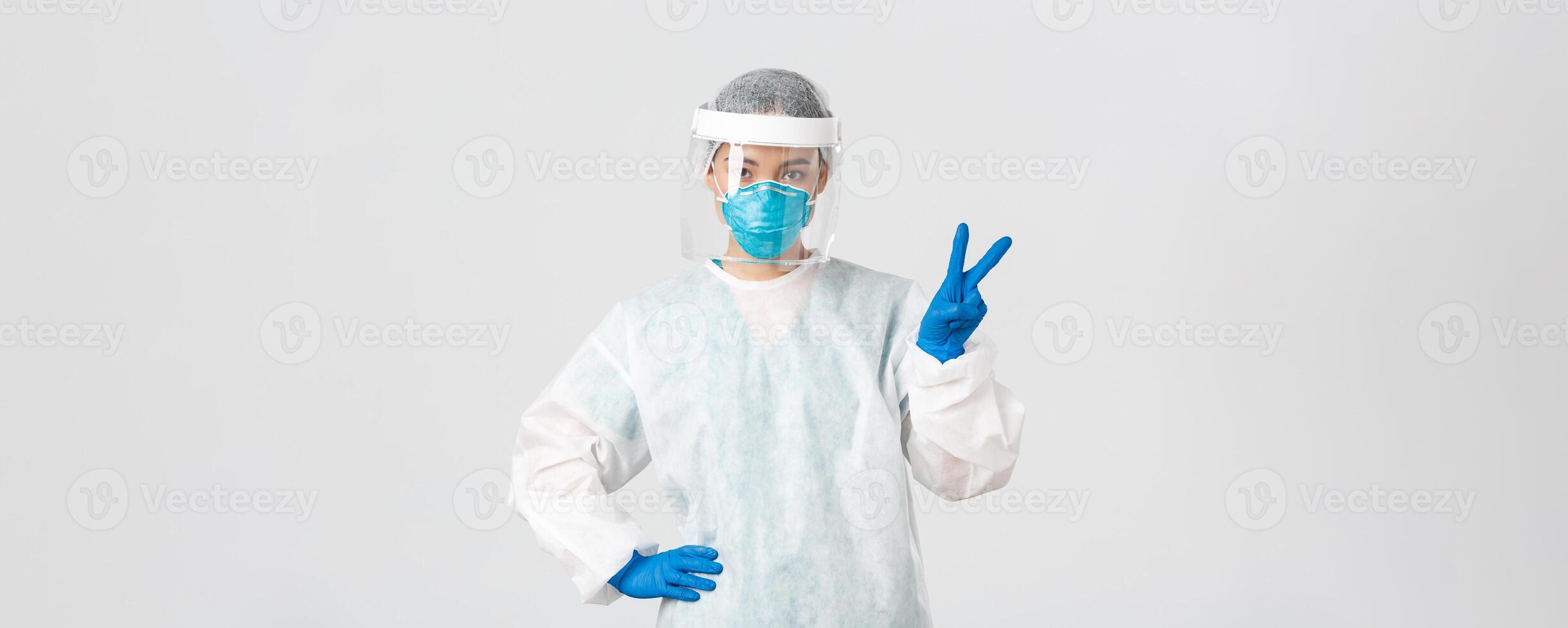 covid19, coronavirus sjukdom, sjukvård arbetare begrepp. sassy asiatisk kvinna läkare, läkare eller tech labb i personlig skyddande Utrustning som visar fred tecken, stående vit bakgrund foto