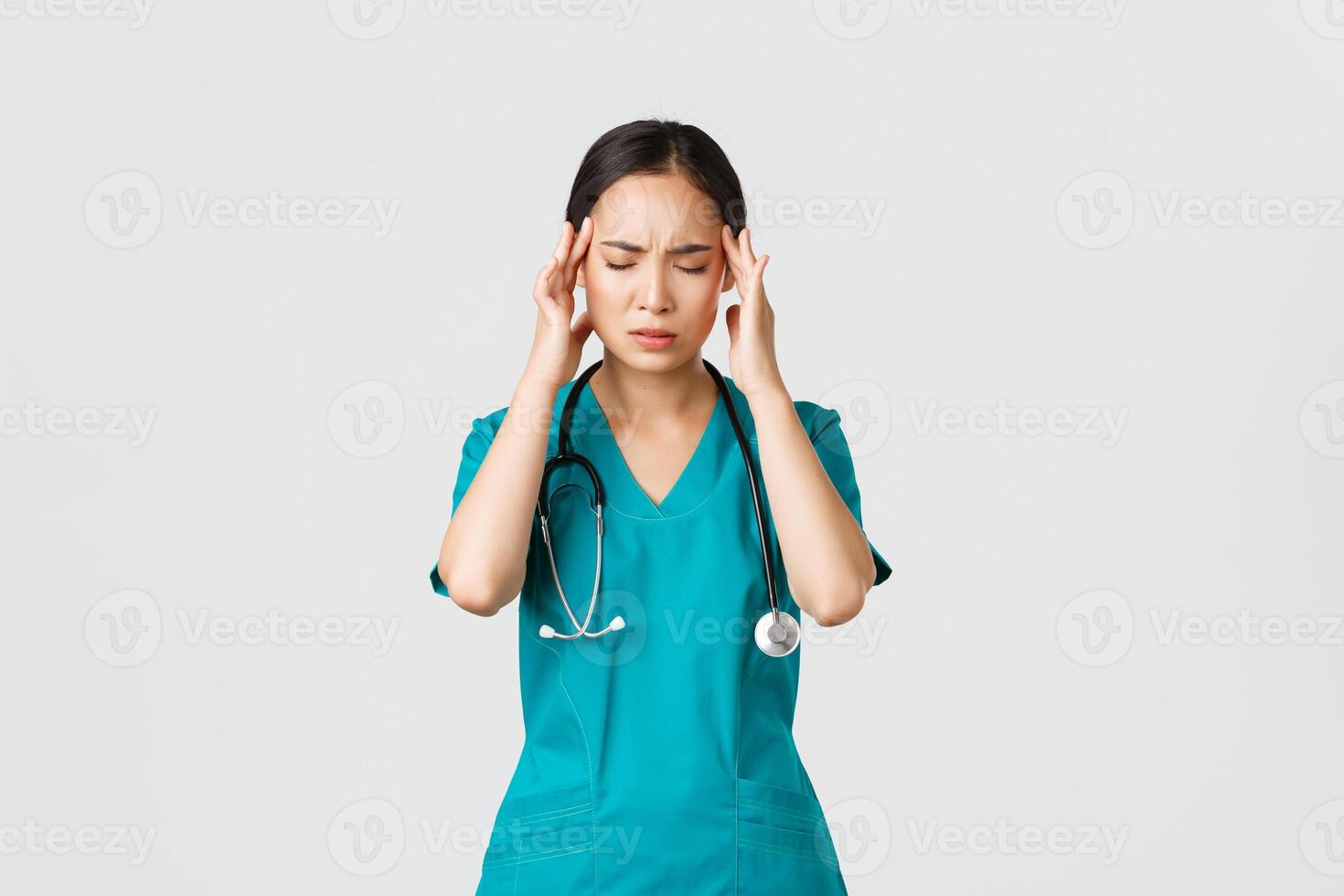 covid19, sjukvård arbetare, pandemi begrepp. överarbetad och trött ung asiatisk kvinna sjuksköterska stänga ögon, grimaserande från huvudvärk, känna yr, natt flytta med coronavirus patienter, vit bakgrund foto