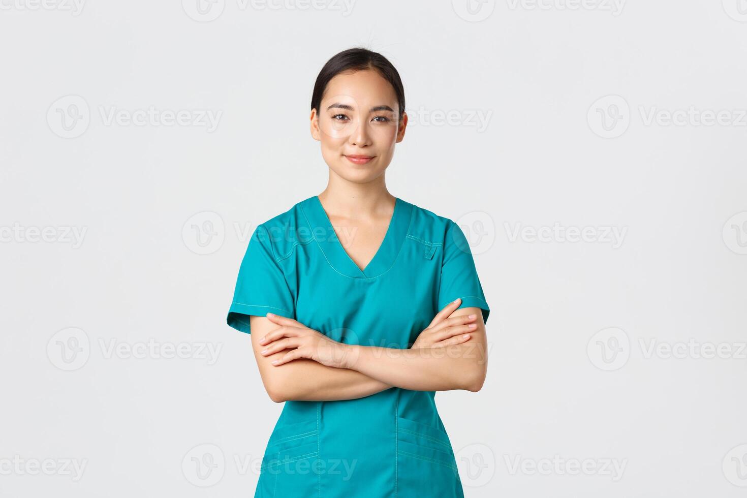 covid19, sjukvård arbetare, pandemi begrepp. självsäker leende asiatisk sjuksköterska i scrubs stående självsäker, korsa vapen bröst. professionell läkare redo för kirurgi, stående vit bakgrund foto