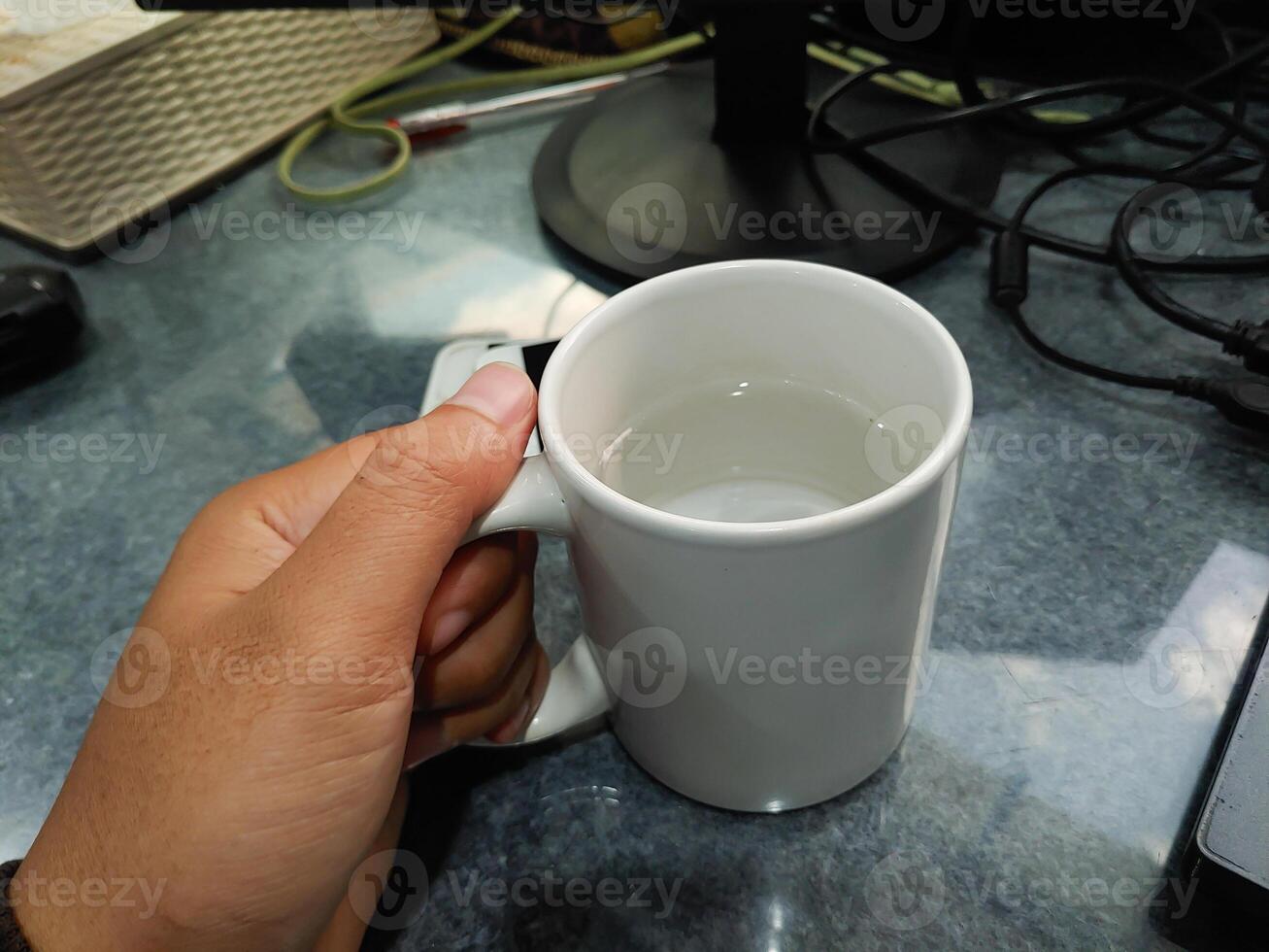 hand innehav kopp med upptagen kontor skrivbord bakgrund. foto