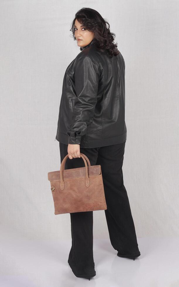 en kvinna i en svart läder jacka och svart byxor med brun läder hand väska foto