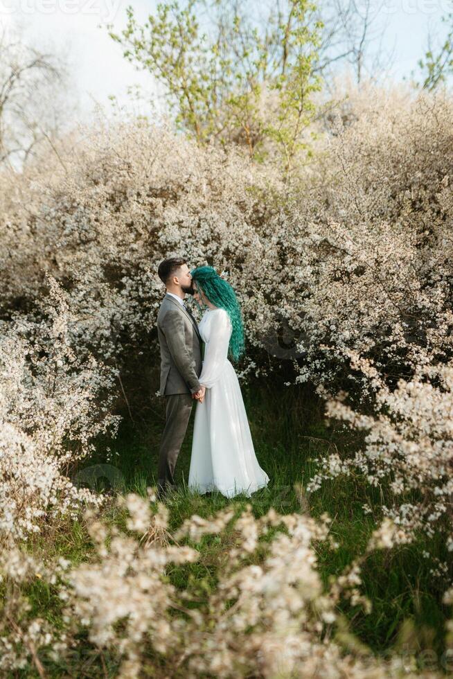 en skäggig brudgum spelar och en flicka med grön hår mot de bakgrund av blomning vår foto