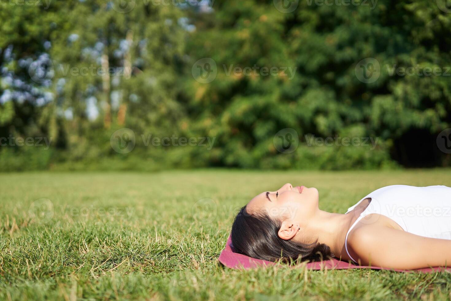 ung kondition flicka liggande på sport matta på gräsmatta, andas och mediterar i parkera i sportkläder foto