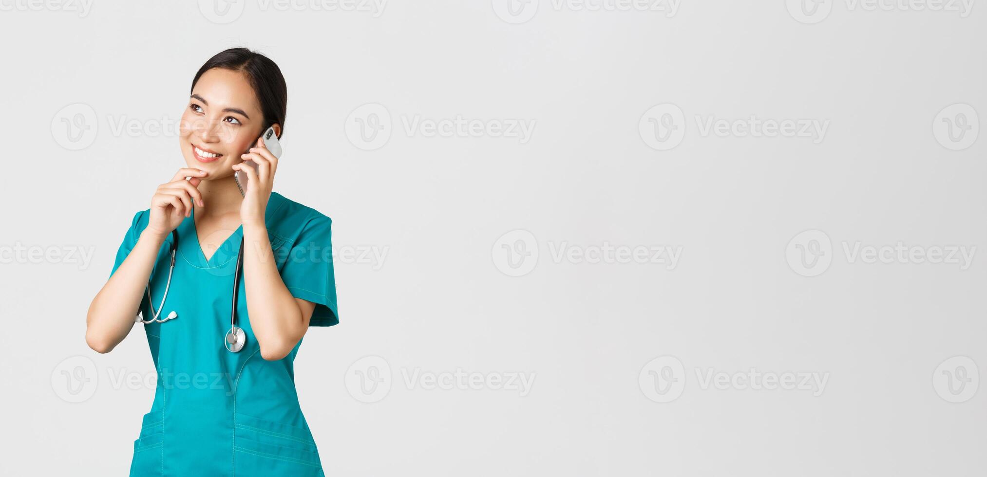 covid19, sjukvård arbetare och förebyggande virus begrepp. porträtt av leende asiatisk kvinna läkare, internera i scrubs talande på telefon och ser omtänksam, tänkande eller framställning val foto