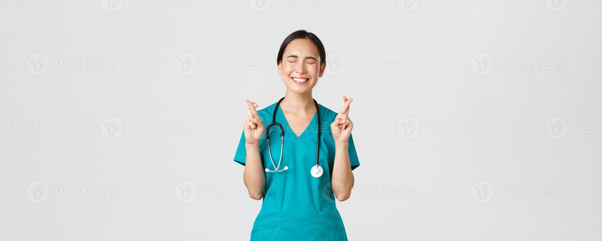 covid19, sjukvård arbetare, pandemi begrepp. optimistisk Lycklig och hoppfull asiatisk kvinna sjuksköterska, internera väntar för befordran, korsa fingrar Bra tur och stänga ögon, leende upphetsad foto