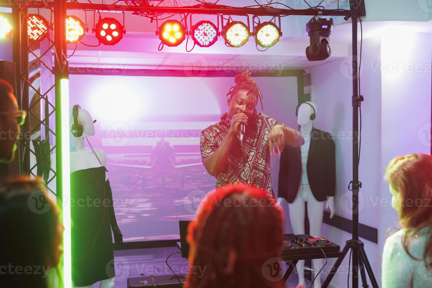 afrikansk amerikan dj sång och spelar på skede under fest i nattklubb. ung man musiker utför och blandning musik på diskotek i klubb med spotlights på natt foto