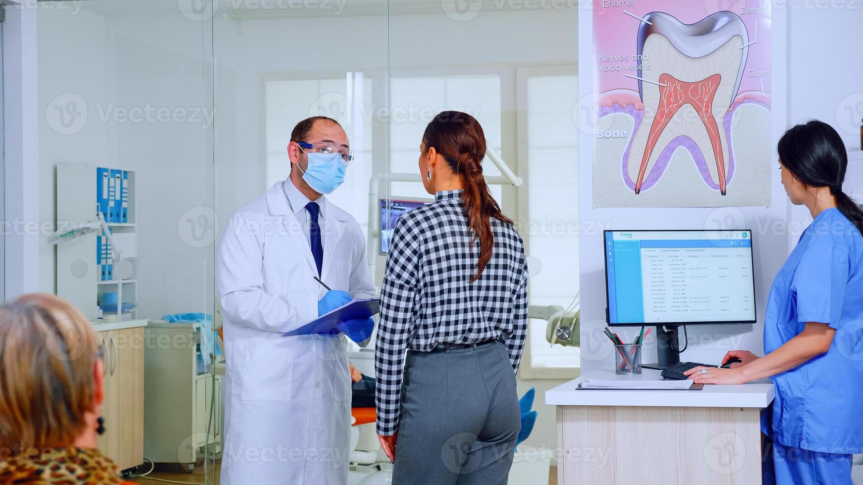 tandläkare läkare förhör kvinna och tar anteckningar på Urklipp stående i väntar område. ung patient förklara dental problem till stomatolog tala i fullt med folk reception av klinik. foto