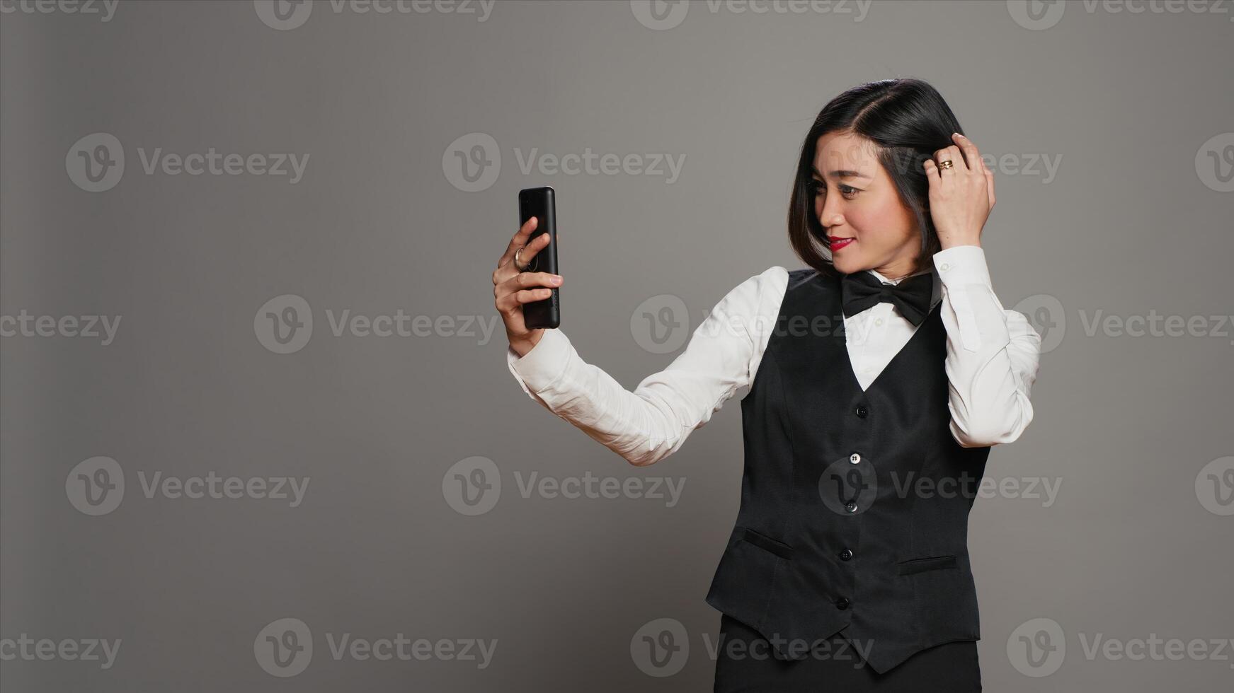 hotell concierge tar foton på smartphone app i studio, har roligt med bilder och arbetssätt som en receptionist. asiatisk främre skrivbord personal använder sig av mobil telefon till fånga dumbom selfies. kamera a.
