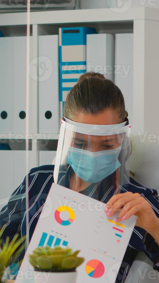 affärskvinna bär ansikte skydd i förebyggande för coronavirus skriver på dator arbetssätt i ny vanligt kontor. frilansare arbetssätt i finansiell företag respekterar social distans under covid-19 foto