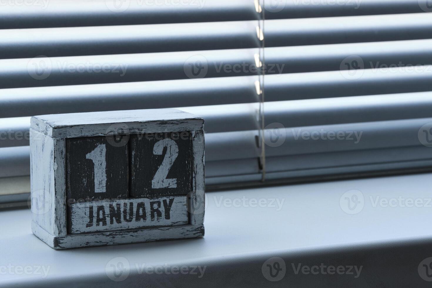 morgon- januari 12 på trä- kalender stående på fönster med persienner. foto