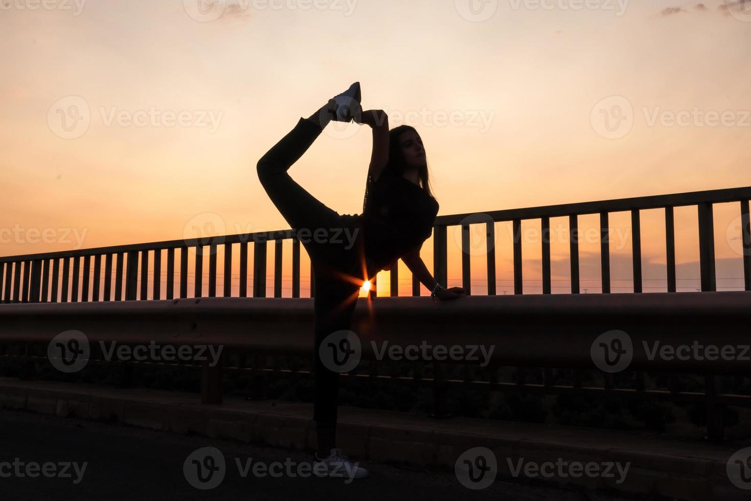 vacker ung brunett flicka poserar en väg i mitten av fältet vid solnedgången, balett, siluett foto