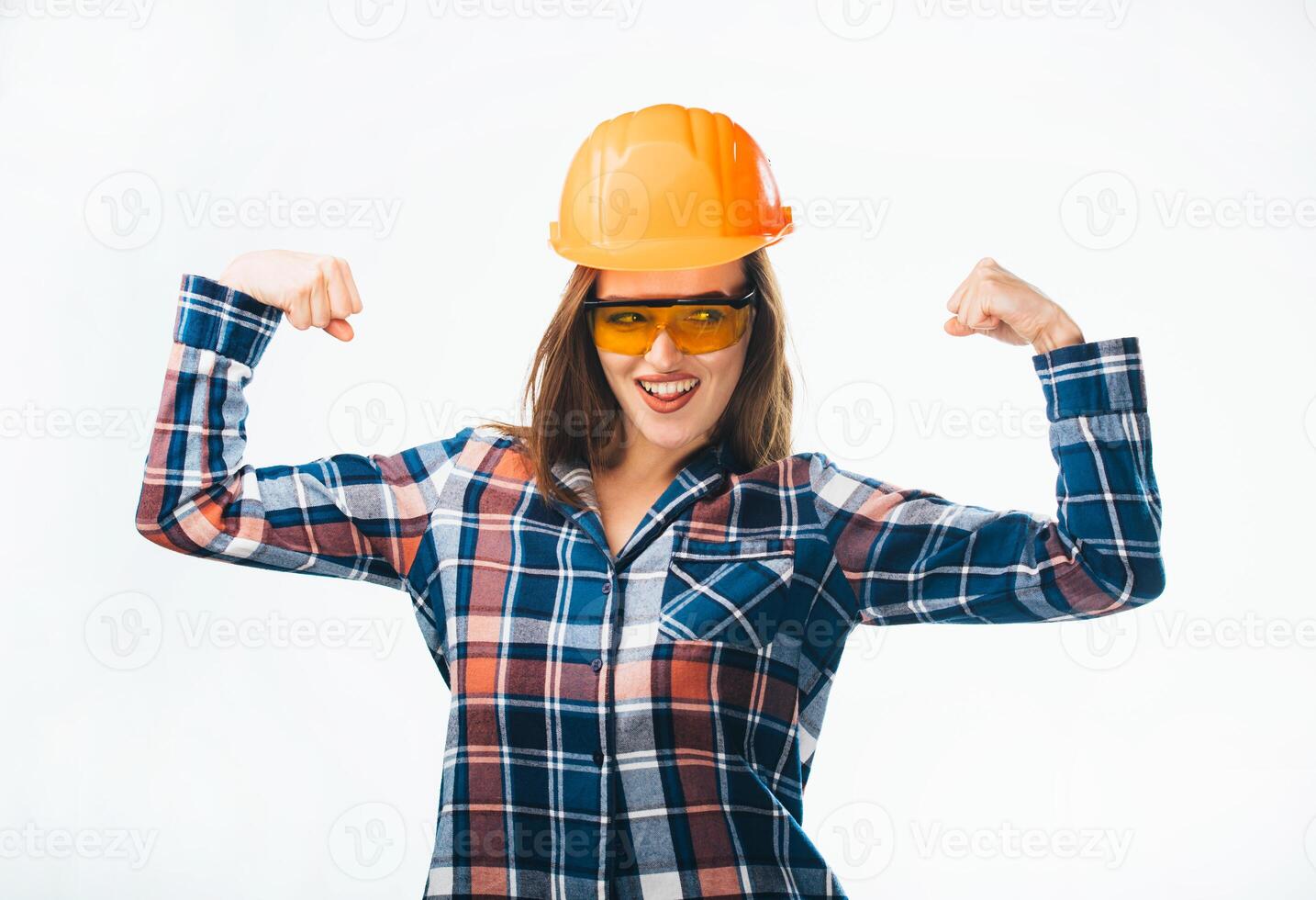 stark ung kvinna i orange hjälm och säkerhet glasögon, pläd skjorta som visar muskler isolerat på vit bakgrund. kvinna manlig arbete. renovering begrepp foto