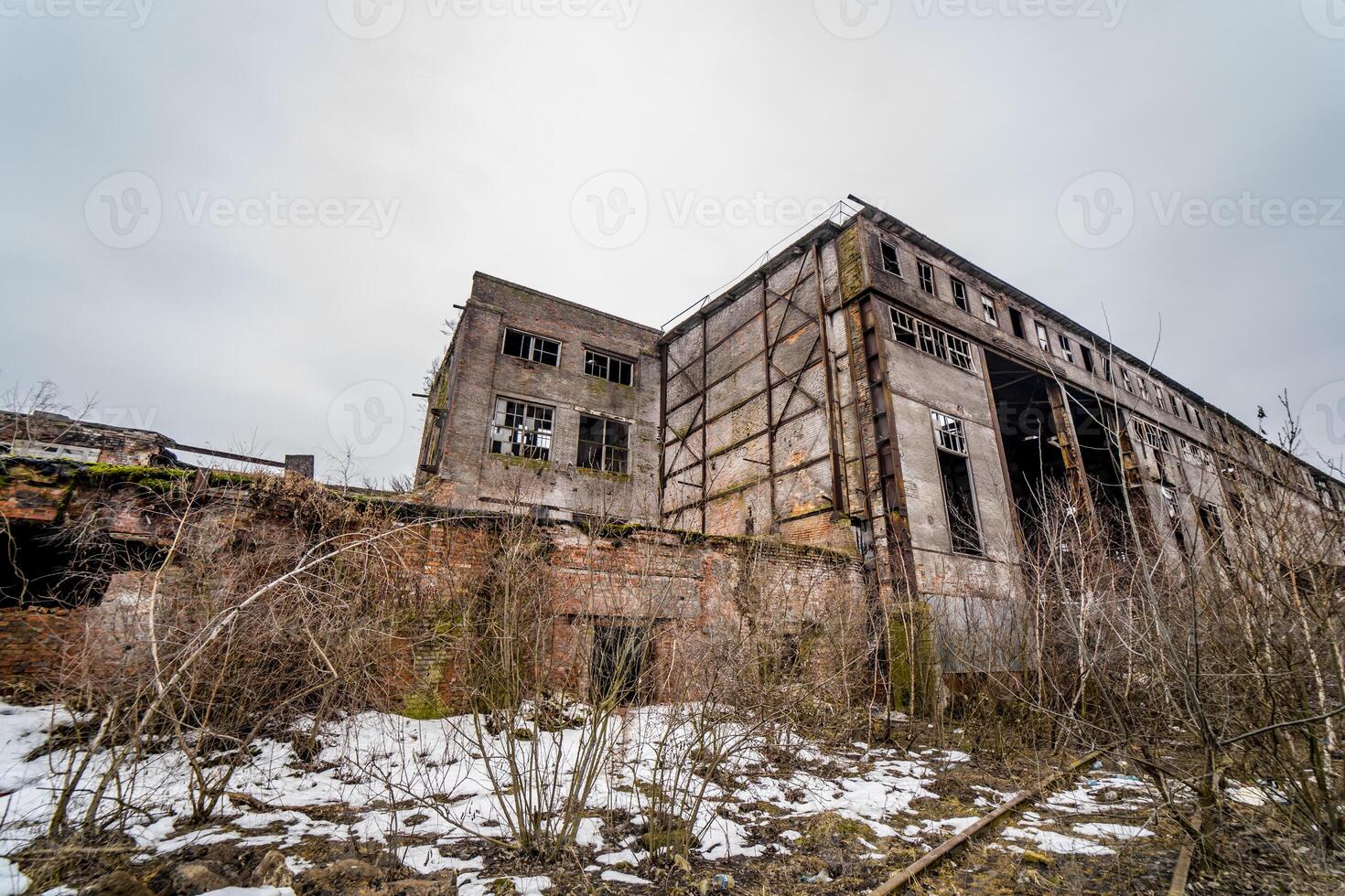 förstörd fabrik eller övergiven lager hall med bruten fönster och dörrar utanför i vinter. resterna av de förstörd industriell byggnader på de snöig bakgrund. foto