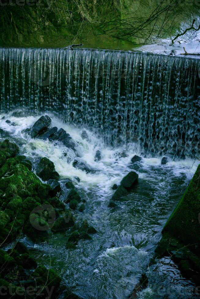 lugn vattenfall cascading över en klippig avsats in i en lugn slå samman omgiven förbi frodig grönska. foto