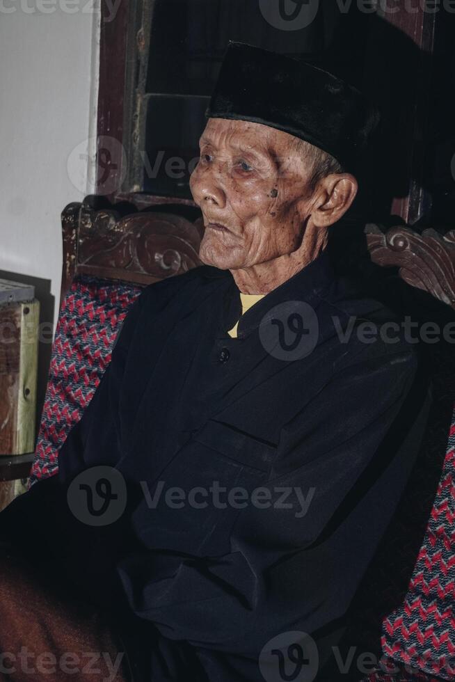 omtänksam senior asiatisk man Sammanträde på Hem soffa, ser bort med tankar, tänkande över framtida pensionering, planera, drömma foto