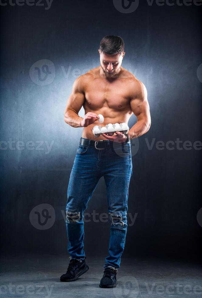 kroppsbyggare ung sportsman är innehav en förpackning med ägg, friska mat protein, grå bakgrund. ser ner på ett ägg. naken torso, friska liv begrepp. foto