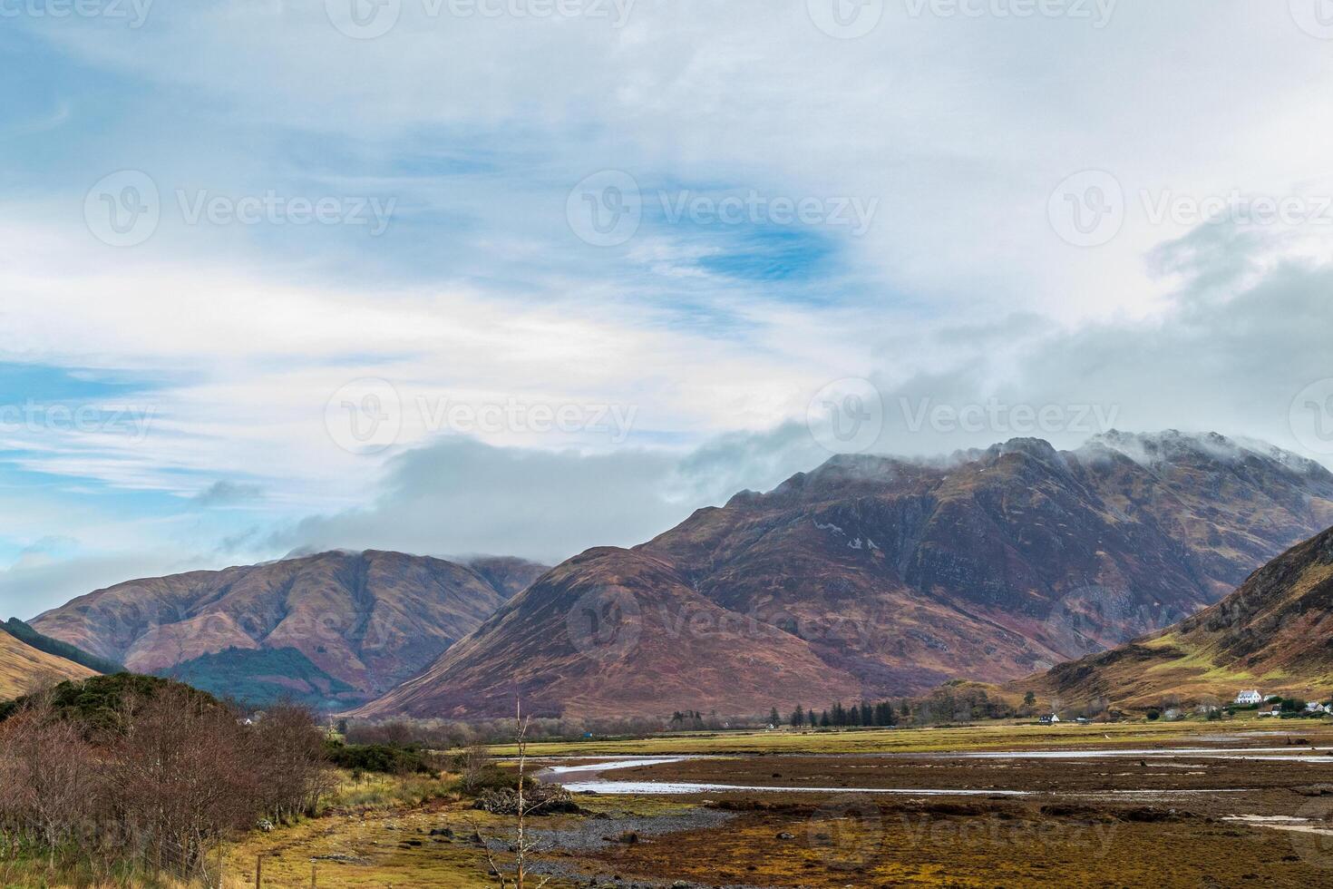 naturskön se av en berg räckvidd med frodig grönska och en molnig himmel, reflekterande i en lugn vatten kropp i de dal i Skottland. foto